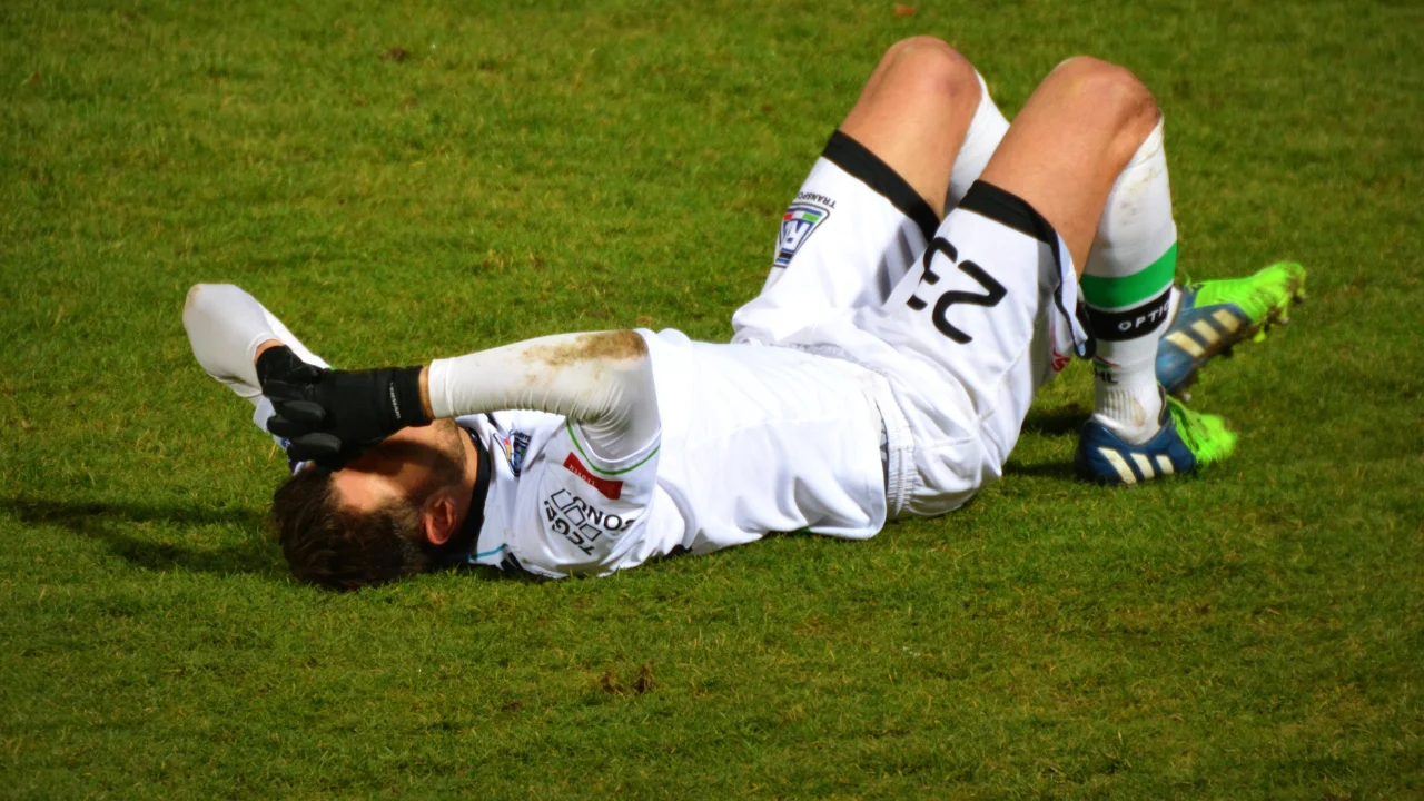 Young man on a football field falling down because of ankle hurt after a sports injury, in Dhaka